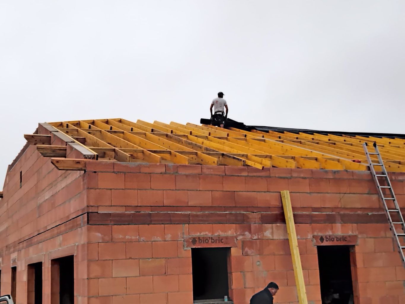 Ecran sous toiture Un ouvrier monte sur un toit en construction, entouré de matériaux de bâtiment.